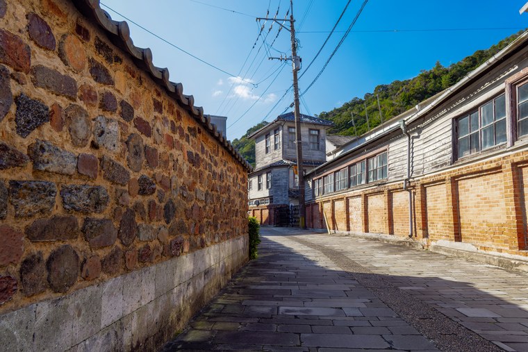 A stone-paved lane in Arita running between a tonbai wall and old wooden workshop buildings