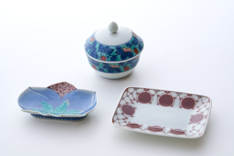 Three Arita pieces: a lidded bowl in blue, a pale lilac leaf-shaped dish, and a rectangular plate with red roundels