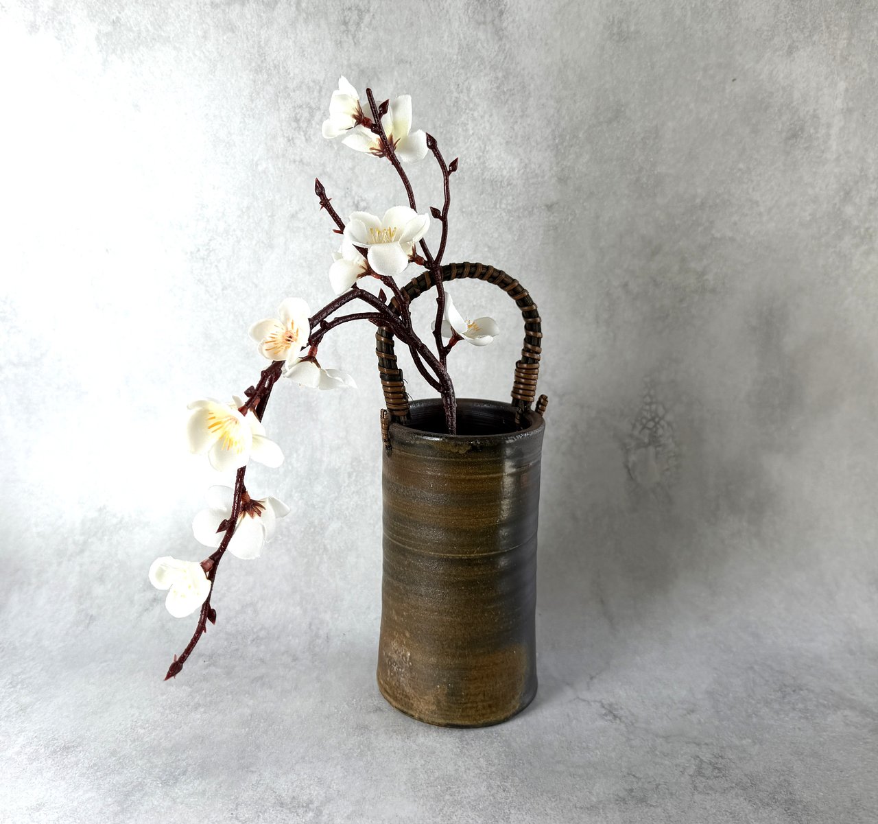 A Bizen flower vase holding a single branch of white plum blossom