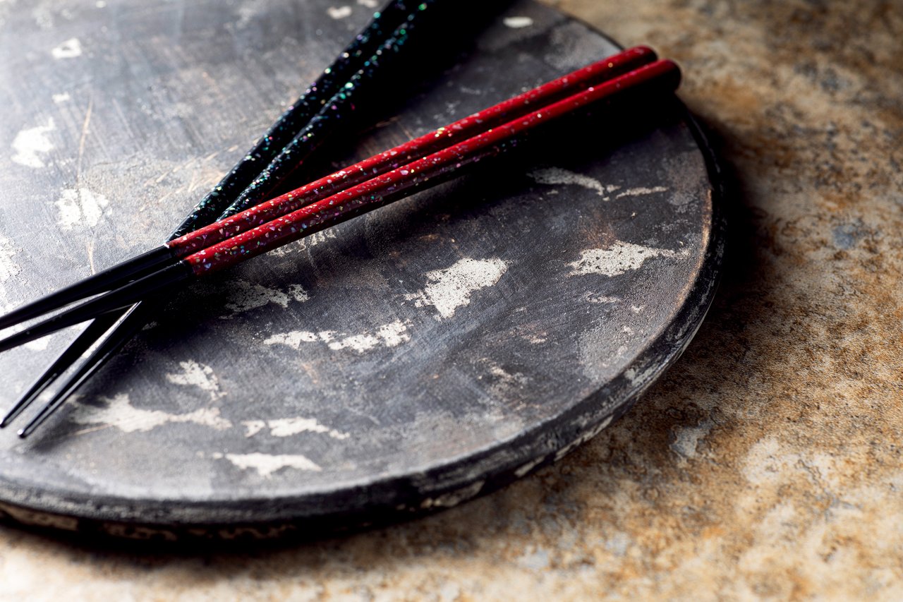 A black and a red lacquered chopstick pair with seashell inlay resting on a stone plate