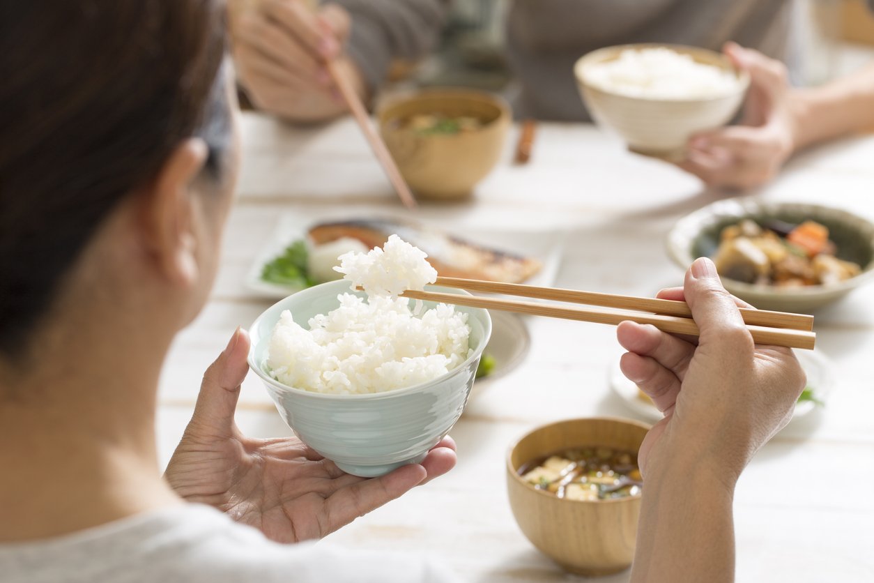 A person lifting rice from a raised rice bowl with wooden chopsticks at a Japanese family table