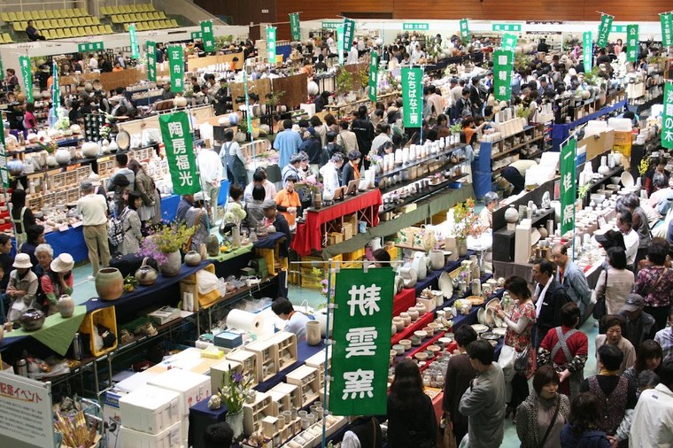Rows of Hagi-ware pottery for sale at a ceramics market, with visitors browsing the stalls