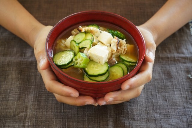 Two hands cradling a red lacquered bowl of miso soup at a home table