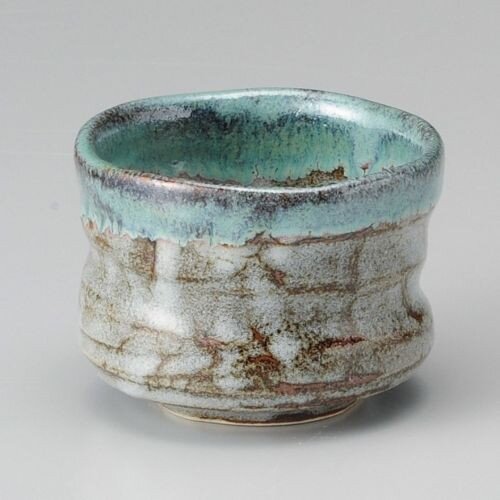 A small Mino ware tea bowl with a turquoise glaze at the rim running over a pale, streaked body