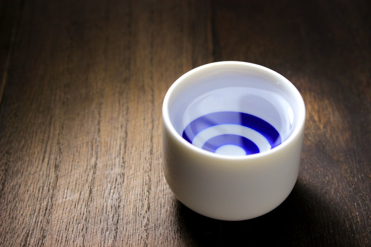 A small white porcelain ochoko with the classical janome cobalt-and-red concentric rings on the inside base — the cup of formal sake tasting