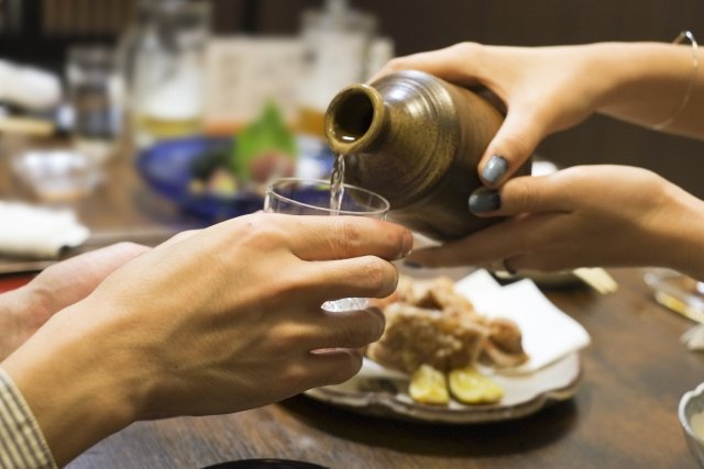 Warm sake being poured from a tokkuri into a small ceramic ochoko, faint steam rising — the moment when the temperature speaks to the vessel