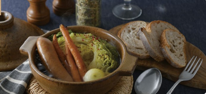 A Shigaraki-ware donabe on the table, filled with a simmering soup, sliced bread on the side