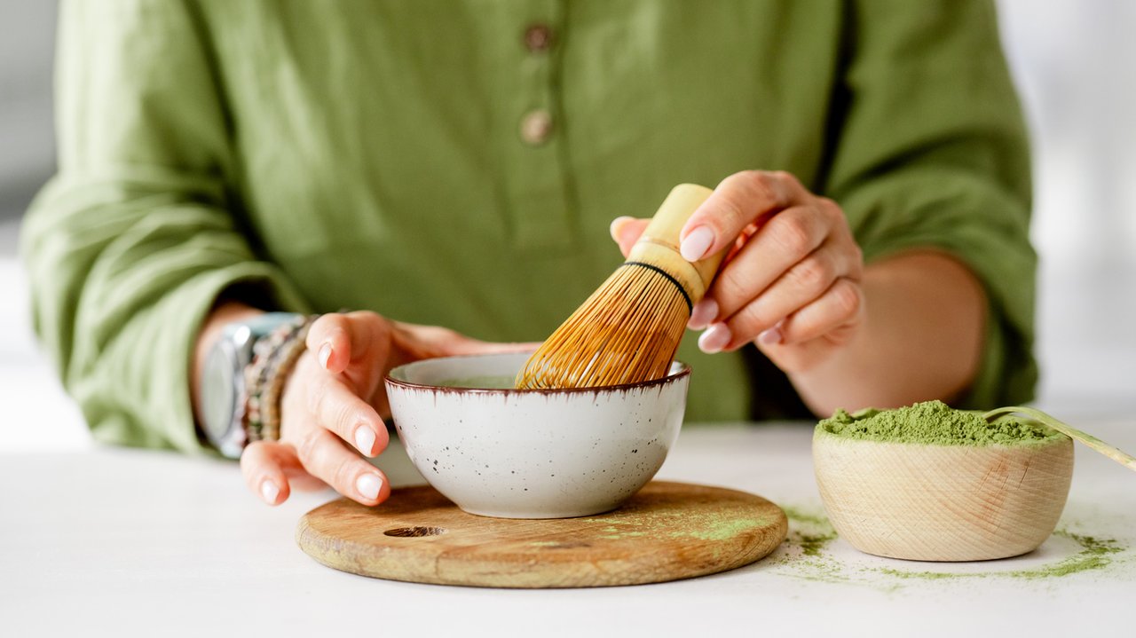 Whisking matcha with a bamboo chasen in a bowl at a bright kitchen table
