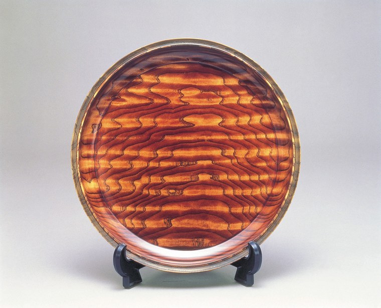 A round Yamanaka tray finished in translucent amber-red lacquer, through which the grain of the wooden base is clearly visible
