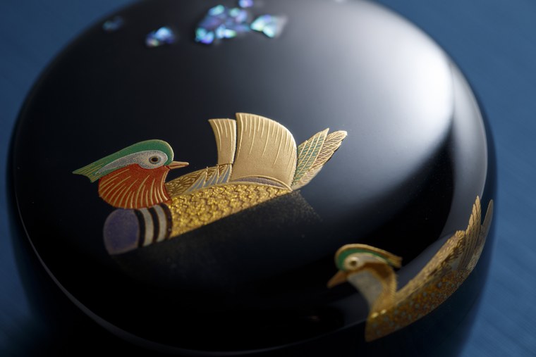 Close view of a black lacquered lidded vessel decorated with a pair of mandarin ducks in gold and colored lacquer, with inlaid shell in the ground