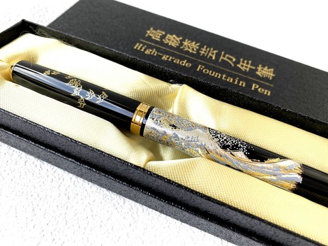 A black fountain pen with a wave breaking along the barrel in silver and gold and small plovers over the cap, lying in its lined presentation box