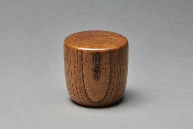 A small turned wooden vessel from Yamanaka with a rounded body and visible grain, unlacquered, against a plain grey ground